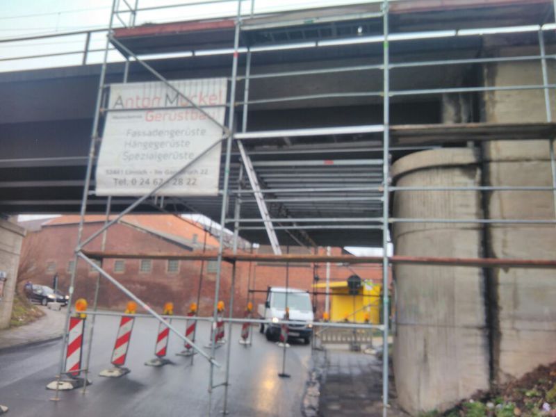 Gerüstkonstruktion neben einem Brückenpfeiler mit dem Banner von Anton Muckel Gerüstbau, dahinter die offene Durchfahrt.